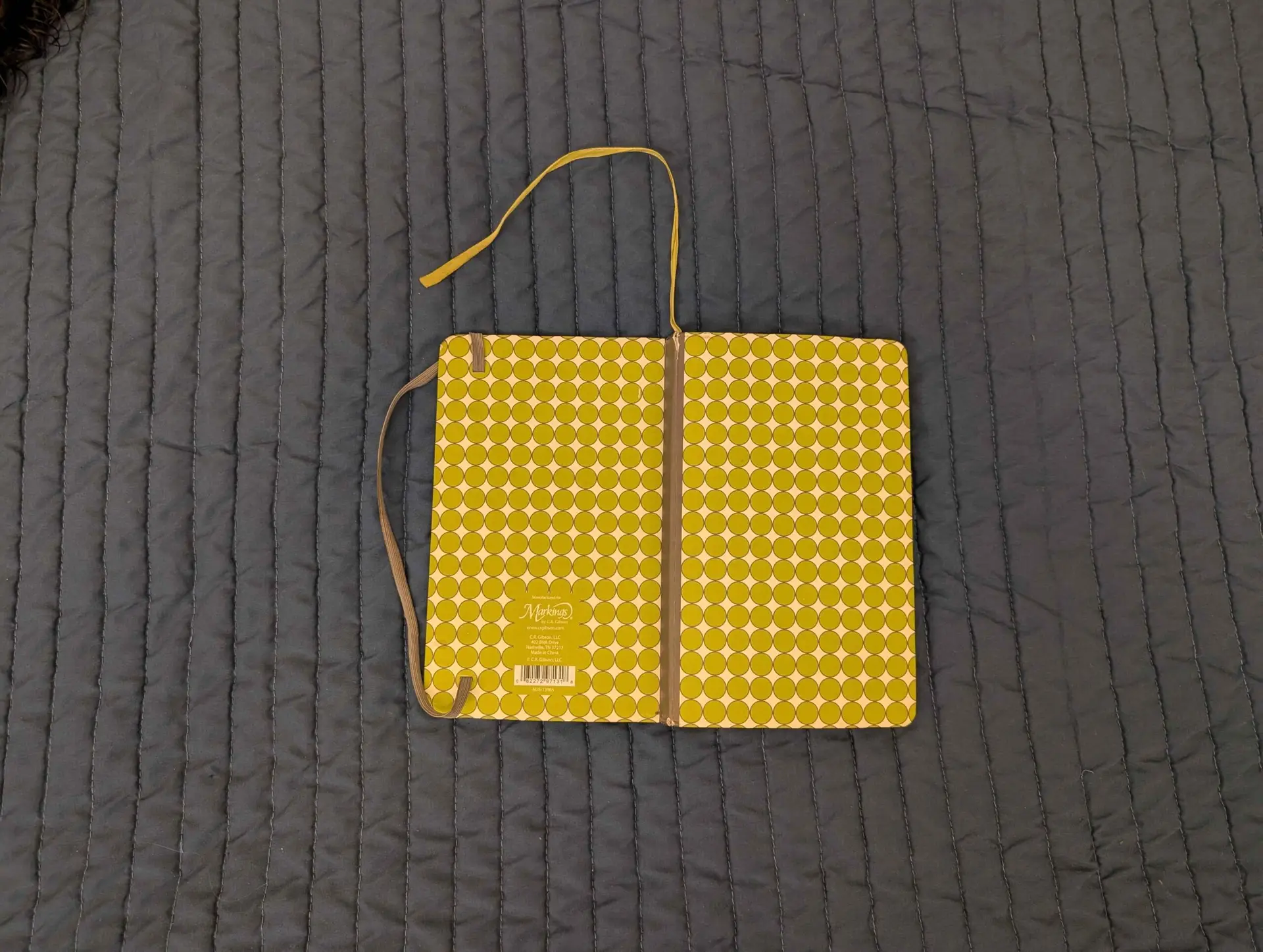 A C.R. Gibson notebook opened on a bed with its spine, cover, ribbon, and clasp showing.