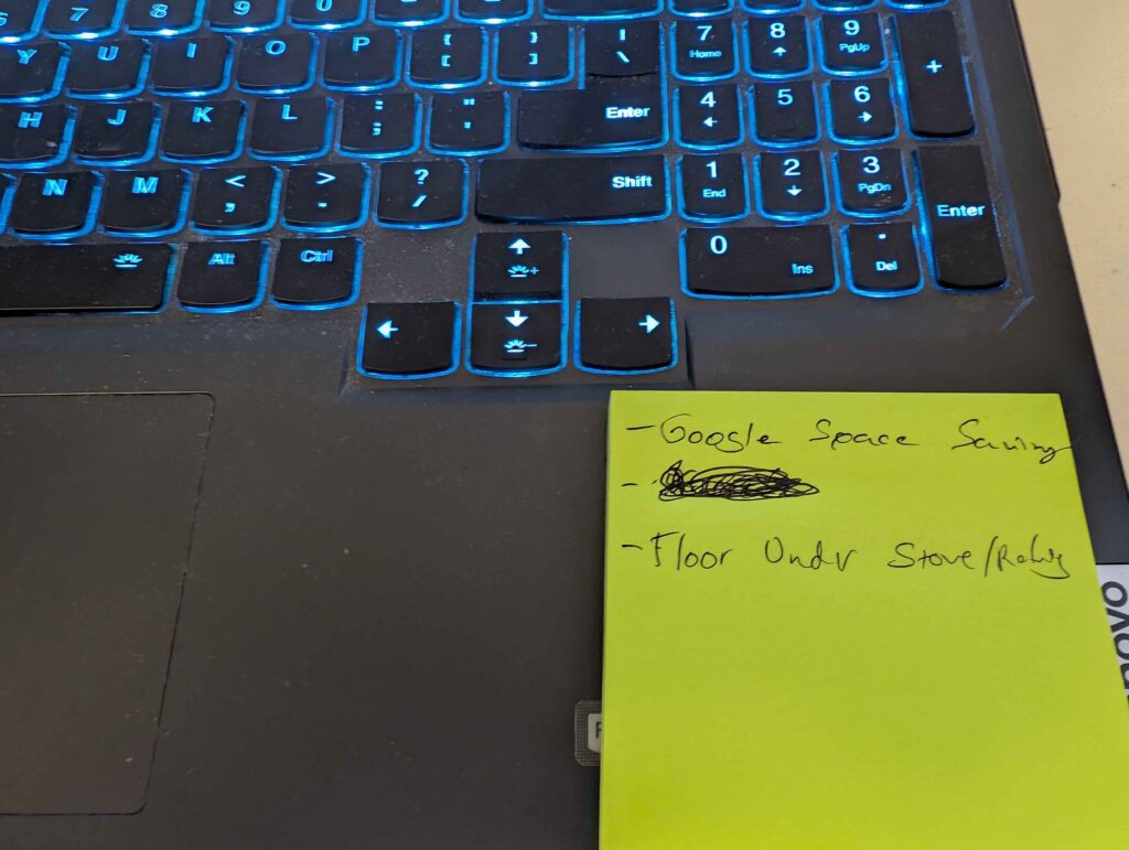 A stick note placed on a laptop, saying to do Google space saving and clean the floor under the stove.
